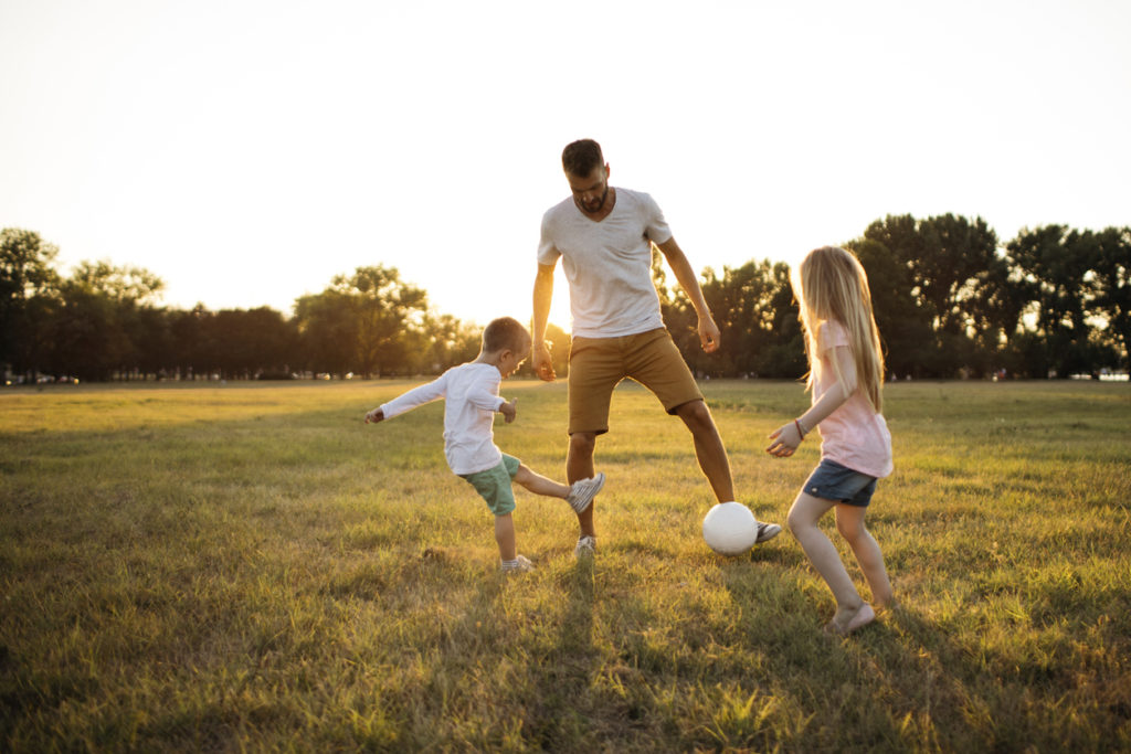 Kids and father playing soccer on a beautiful summer afternoon outdoors