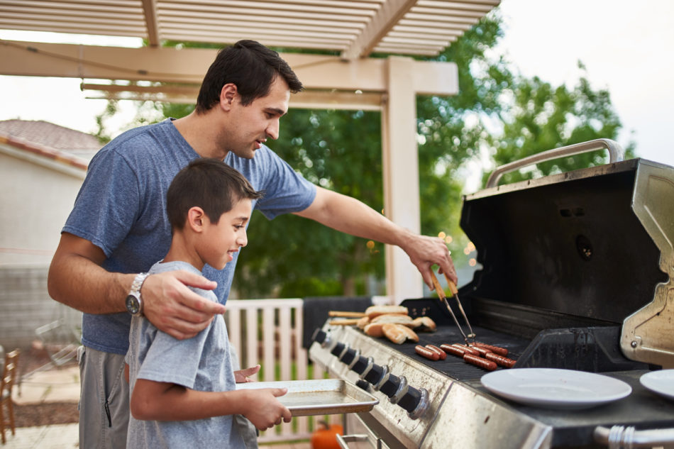 father teaching son how to grill hot dogs