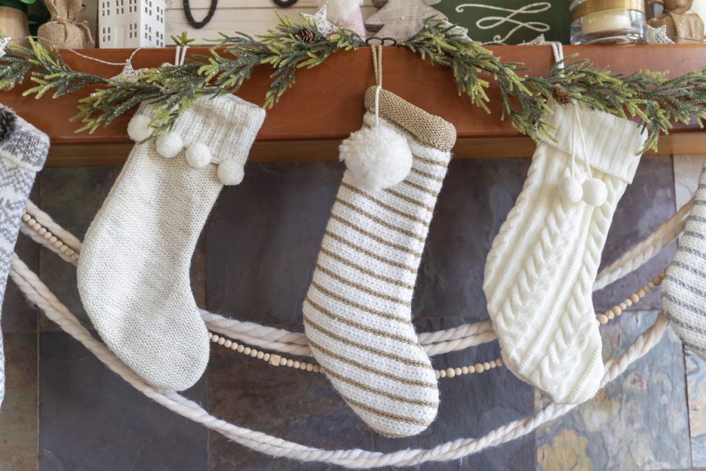 Close up of white Christmas stockings and winter holiday decorations in modern farmhouse Scandinavian design above fireplace in cozy family living room.