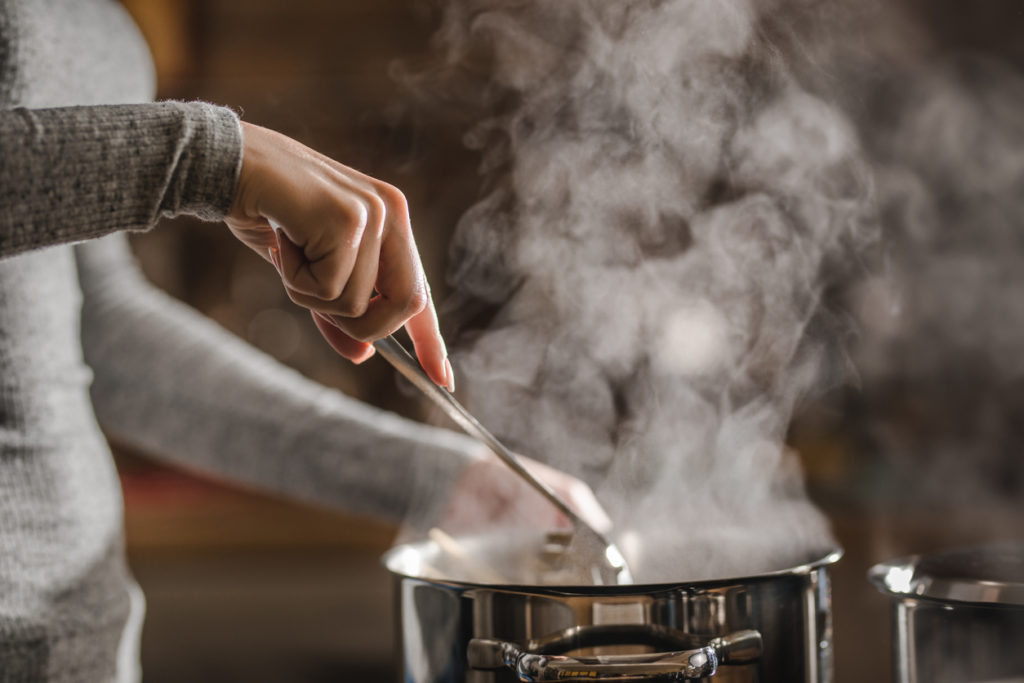 woman stirring soup in a saucepan while making lunch.