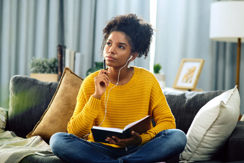 Shot of a young woman listening to music while writing in her notebook