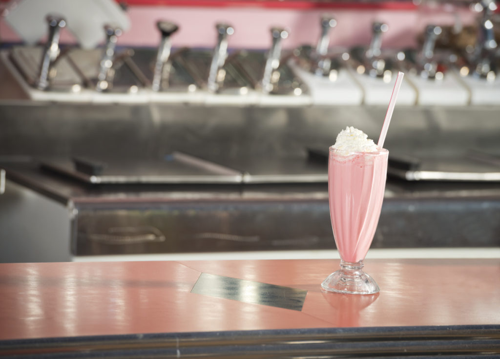 A strawberry milkshake sitting on a counter at a 1950's diner